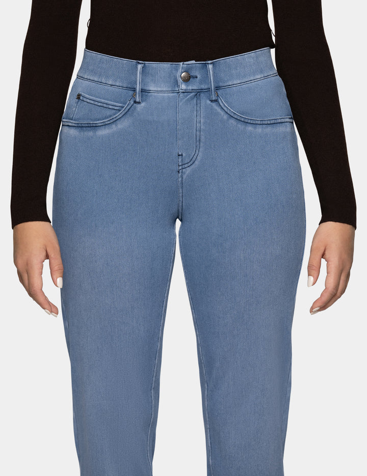 A detailed view of a model wearing light blue denim pants, and a long sleeve black top photographed against a light gray background.