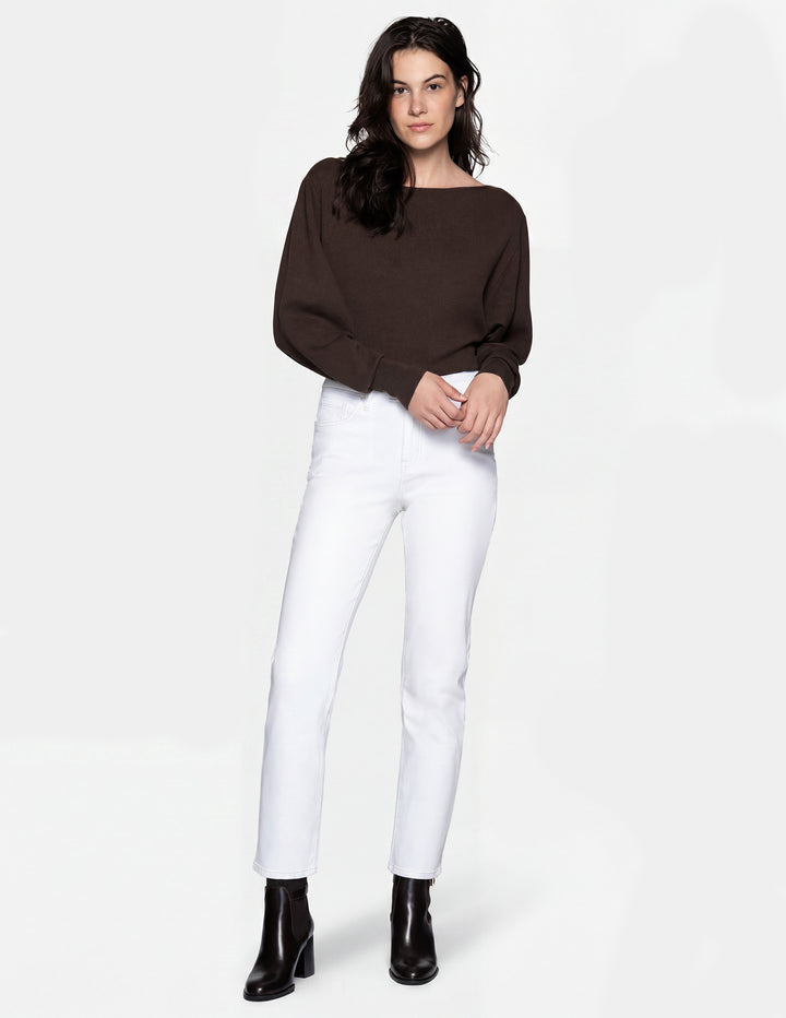 A model wearing white pants, a brown long sleeve top, and black boots photographed against a light gray background.