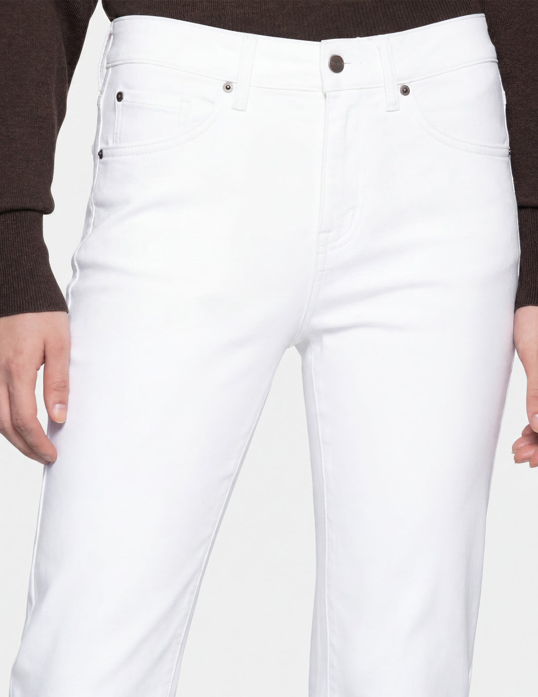 A closeup of model wearing white pants and a long sleeve top photographed against a light gray background.