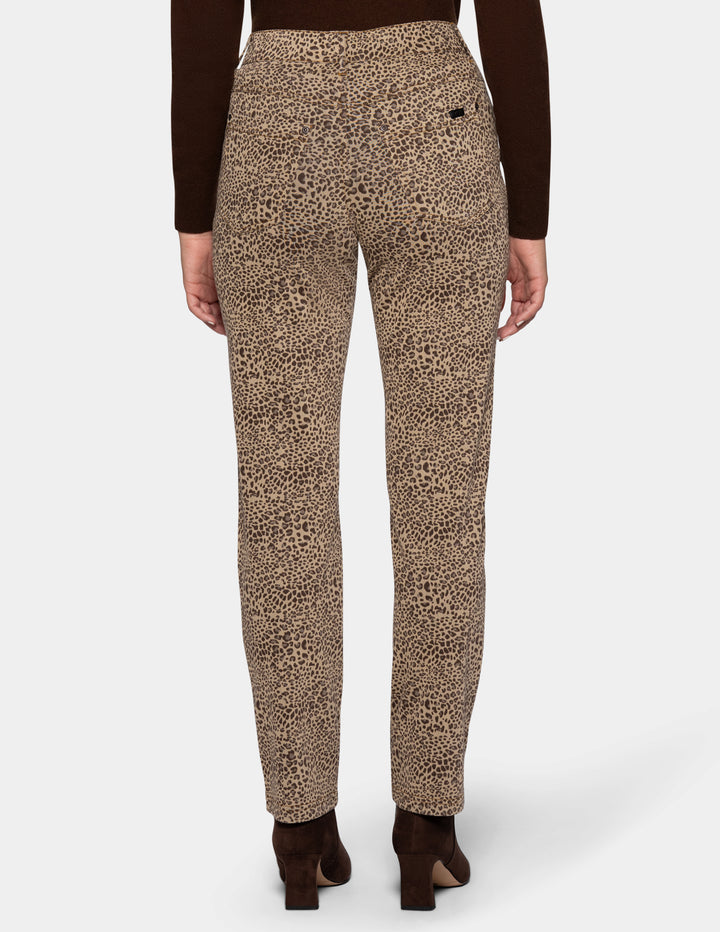 A backside view of a model wearing cheetah pants, a long sleeve brown top, and brown boots photographed against a light gray background.