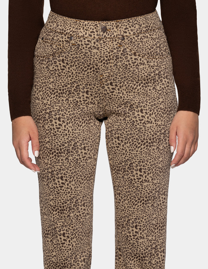 A closeup view of a model wearing cheetah pants, and a long sleeve brown top, photographed against a light gray background.