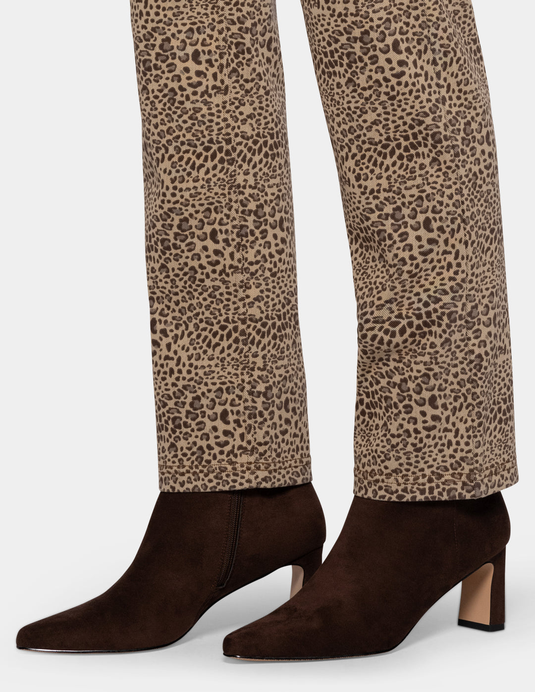 A closeup view of a model wearing cheetah pants, and brown boots photographed against a light gray background.
