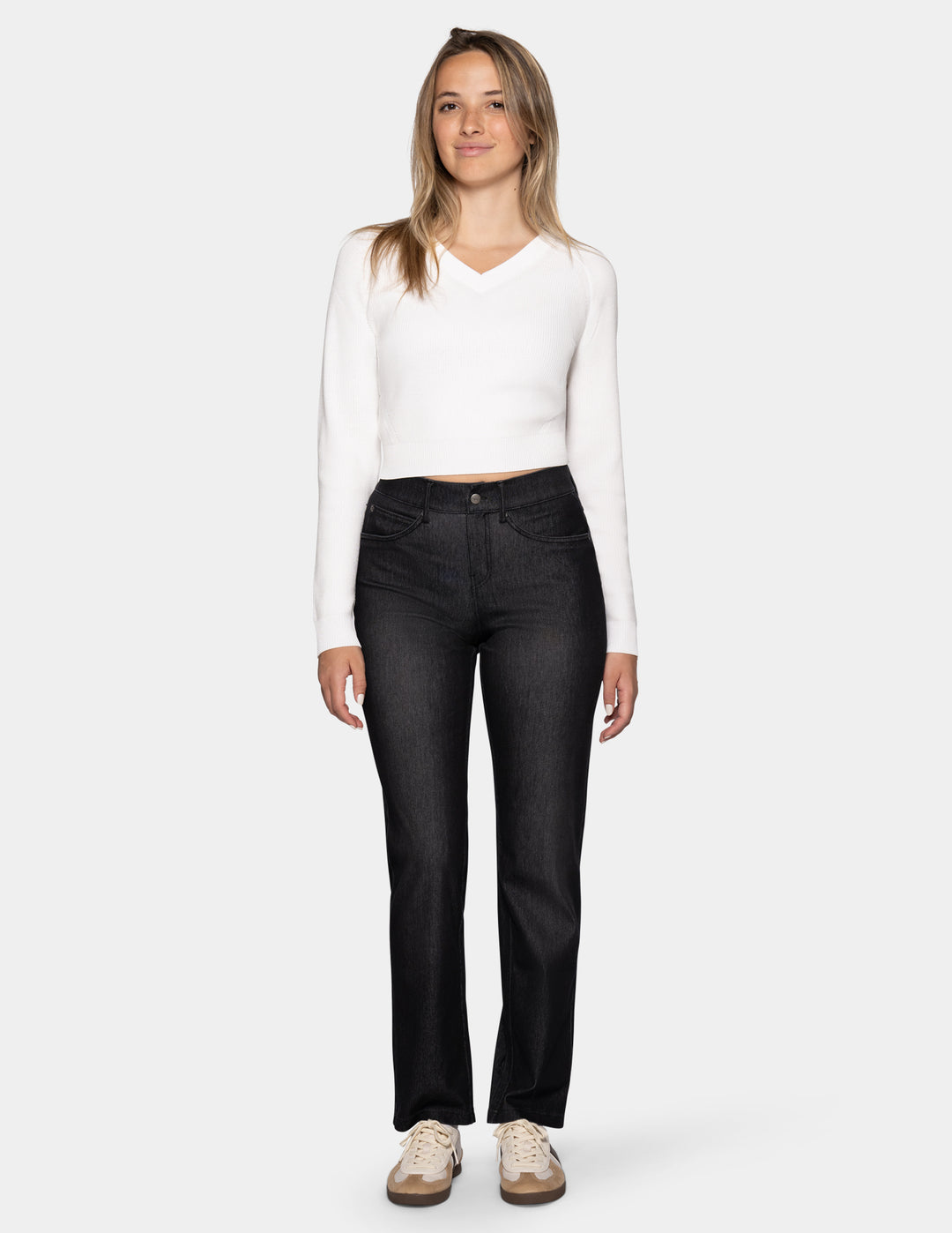 A model wearing black denim pants, a long sleeve white top, and sneakers photographed against a light gray background.
