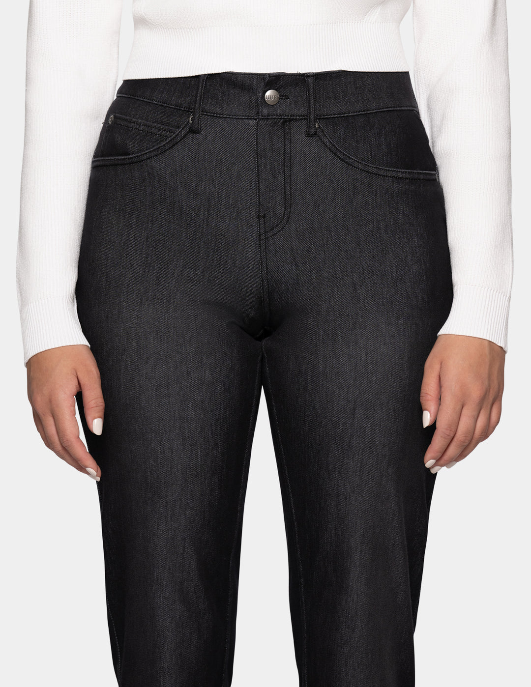 A detailed view of a model wearing black denim pants, a long sleeve white top, and sneakers photographed against a light gray background.