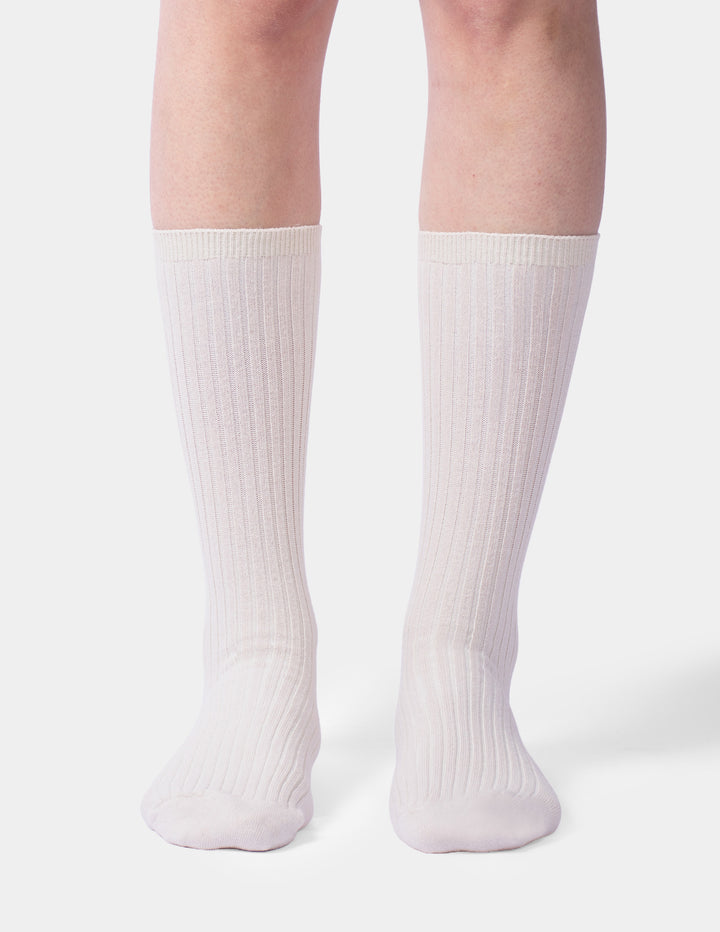 A model wearing a pair of beige crew socks photographed against a light gray background.