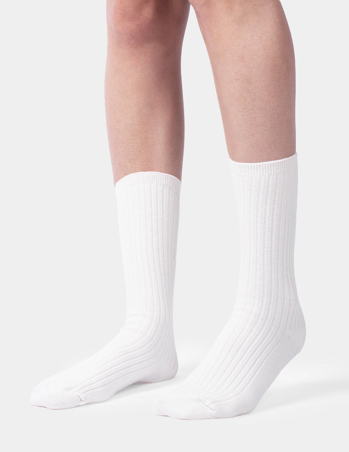 A model wearing an ivory pair of ribbed crew socks displayed against a light gray background.