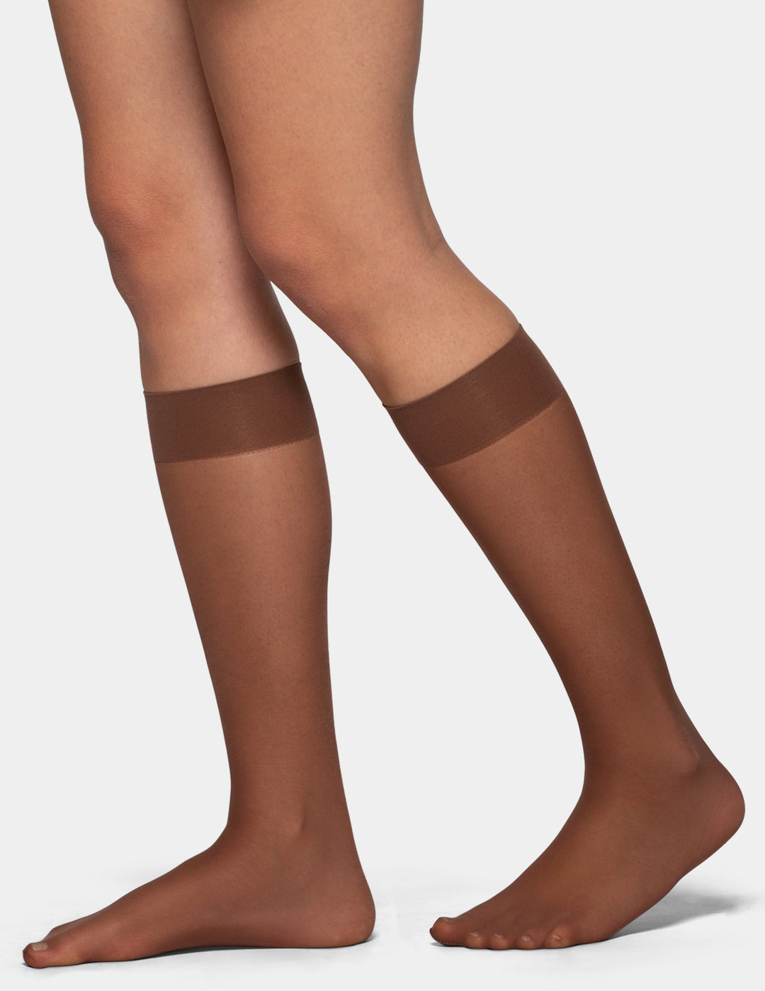 A close-up of a person's legs wearing sheer knee-high stockings with a wide medium-brown band at the upper calf, shown against a light gray studio background.