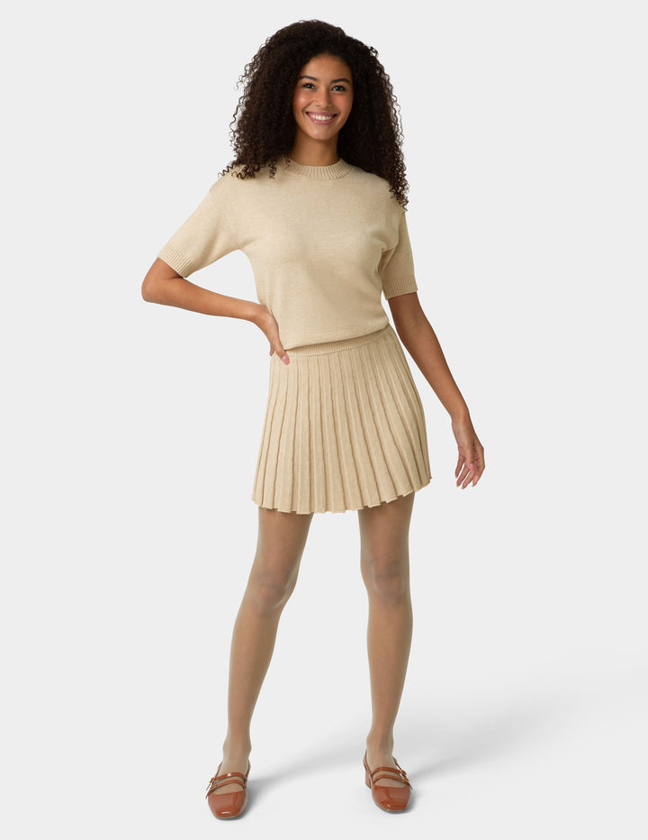 Woman wearing a beige top and pleated skirt on a white background