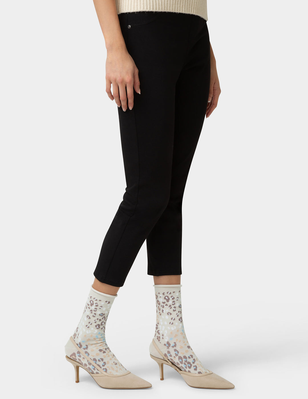 Person wearing black pants and beige high-heeled shoes with pattern socks on a white background