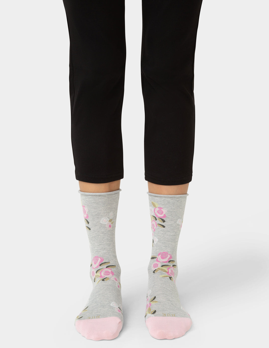 Person wearing gray socks with floral patterns and black pants on a white background