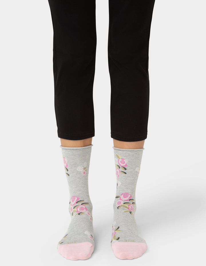 Person wearing gray socks with floral patterns and black pants on a white background