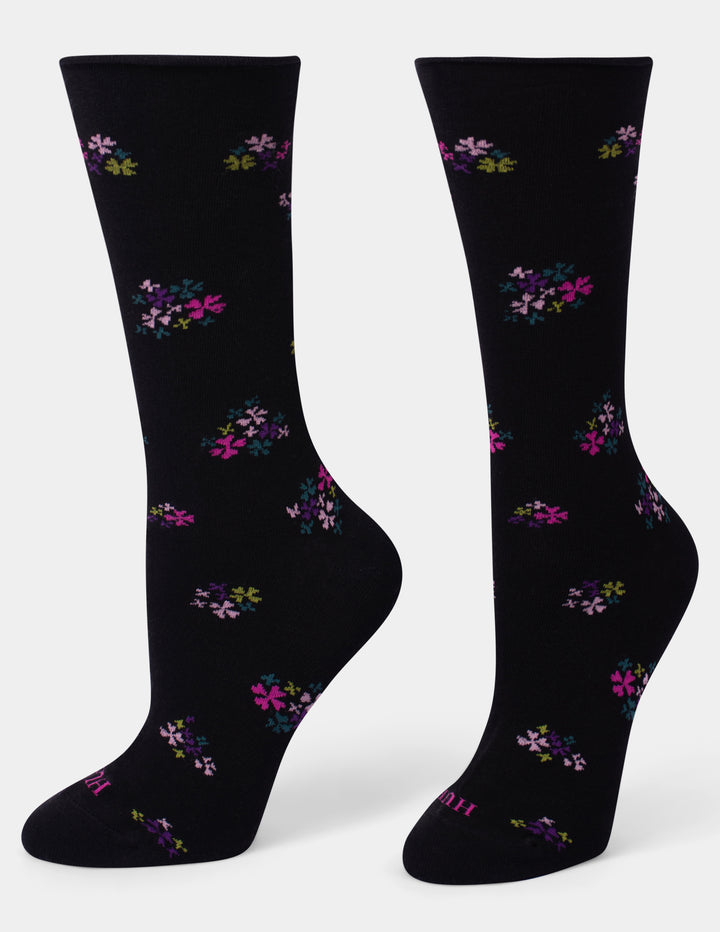 A pair of black crew socks with a scattered floral pattern in pink, purple, and green, displayed against a light gray background.