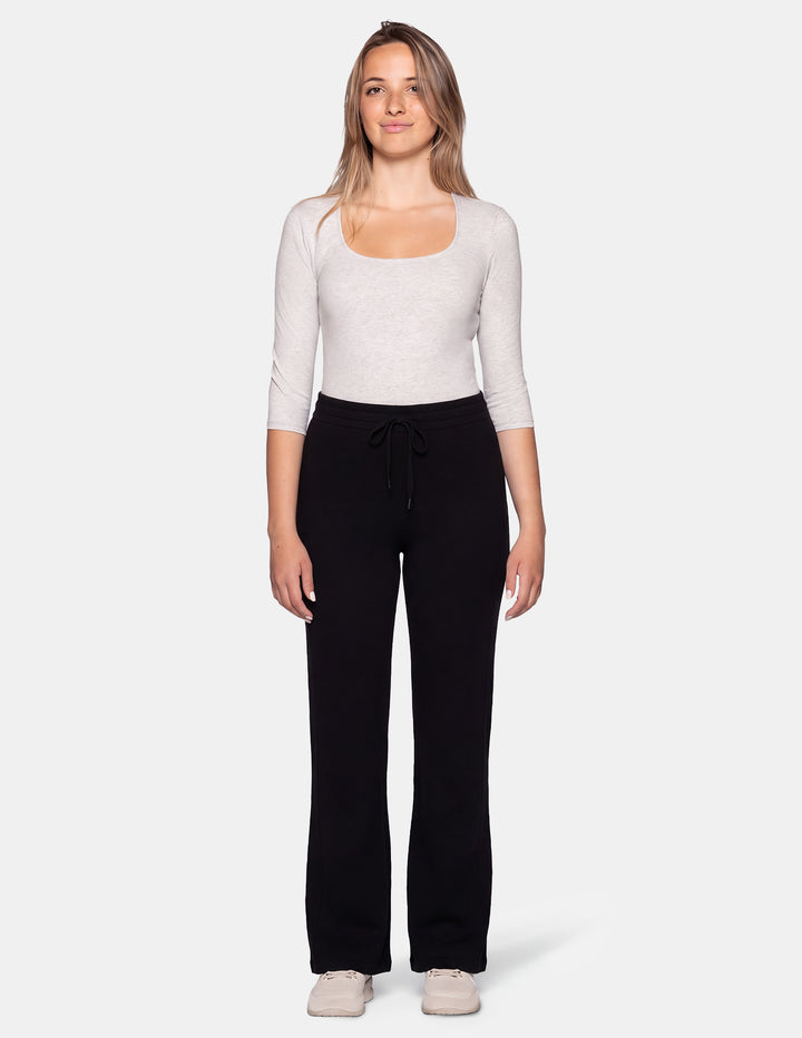 A woman modeling a light heather gray scoop-neck long-sleeve top and black sweatpants against a light gray studio background.