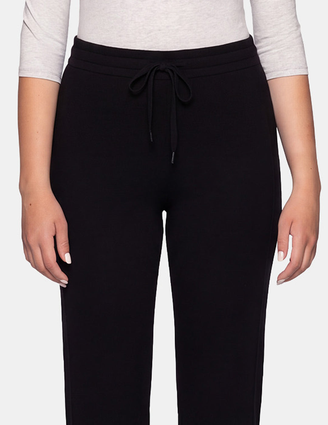 A close-up of a model wearing black jersey trackpants against a gray background.