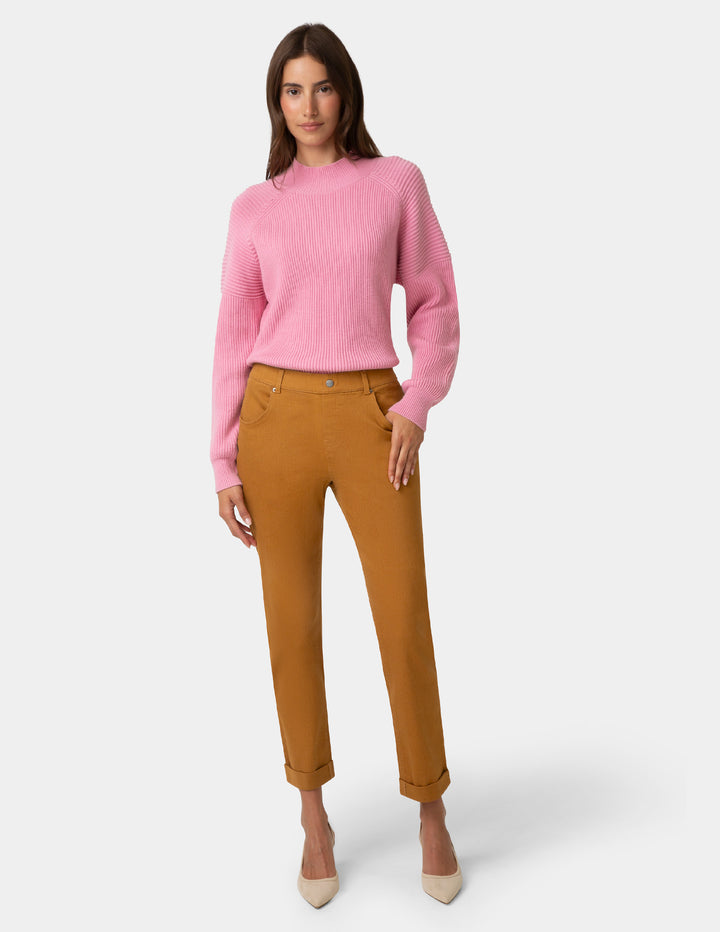 Woman wearing a pink sweater and brown pants on a white background
