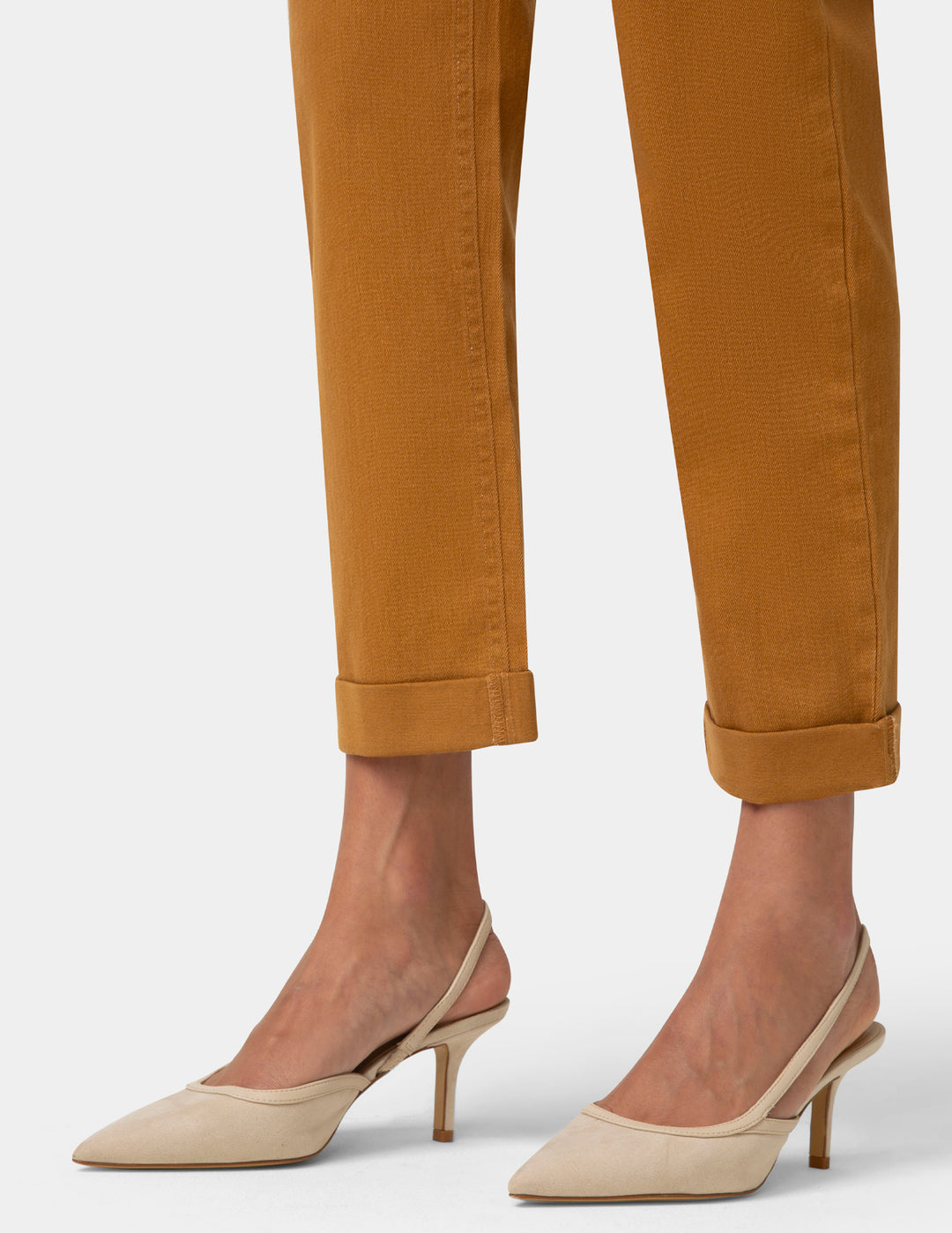 Beige high-heeled shoes worn with mustard yellow pants on a white background