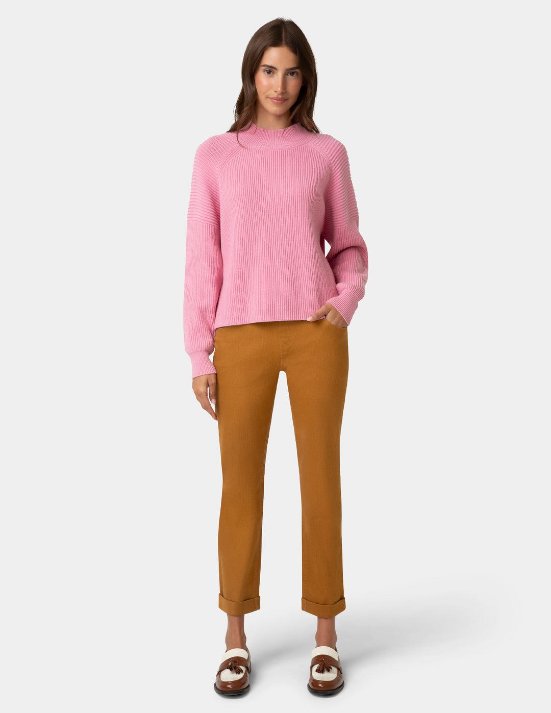 Woman wearing a pink sweater and brown pants on a white background