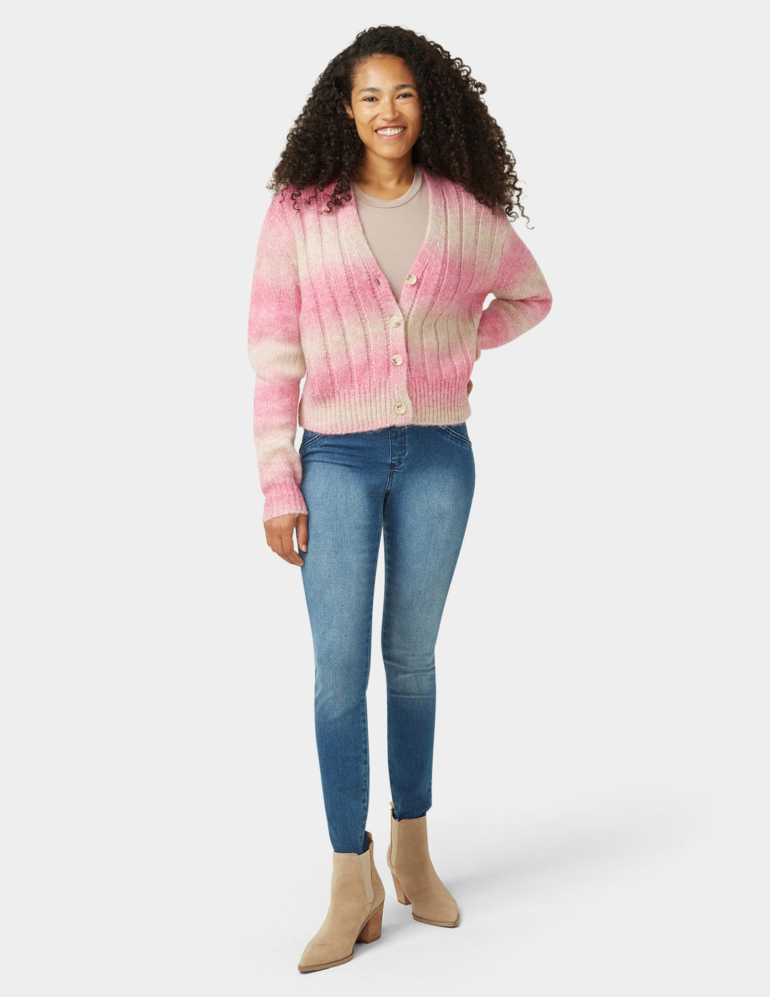 Woman wearing a pink and beige tie-dye cardigan with blue jeans on a white background
