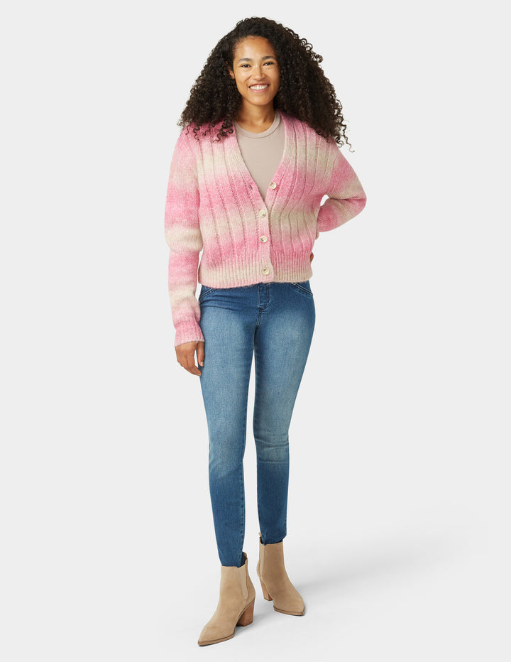 Woman wearing a pink and beige tie-dye cardigan with blue jeans on a white background