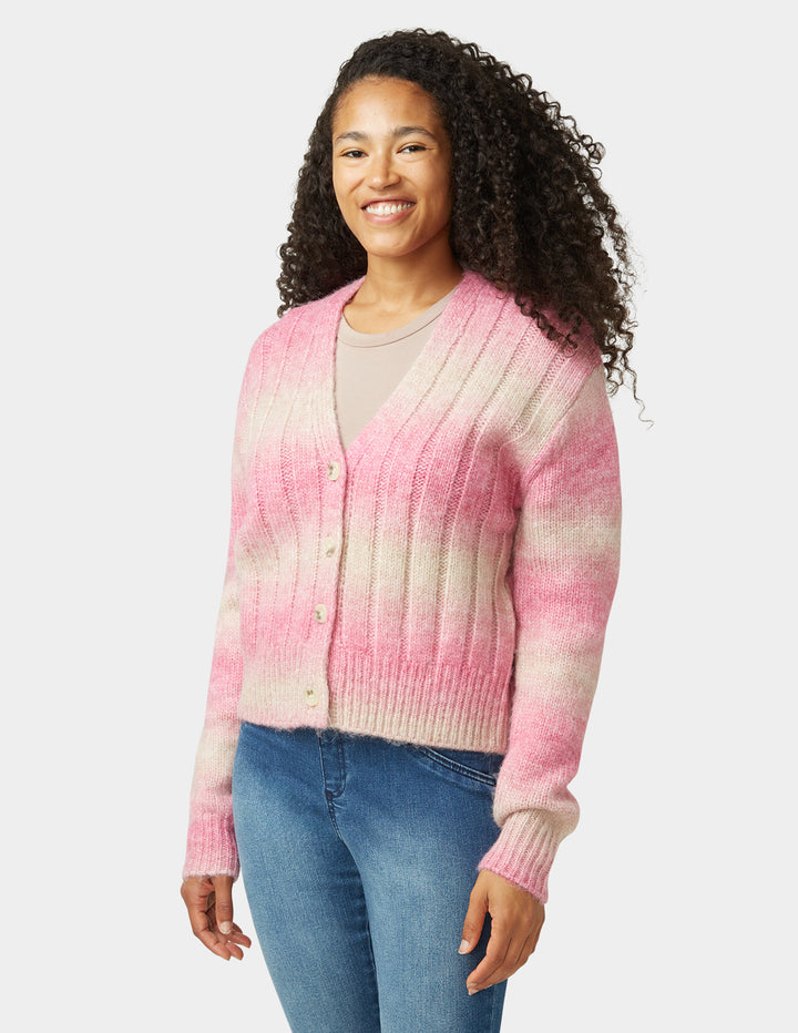 Woman wearing a pink and white gradient cardigan with blue jeans on a light gray background