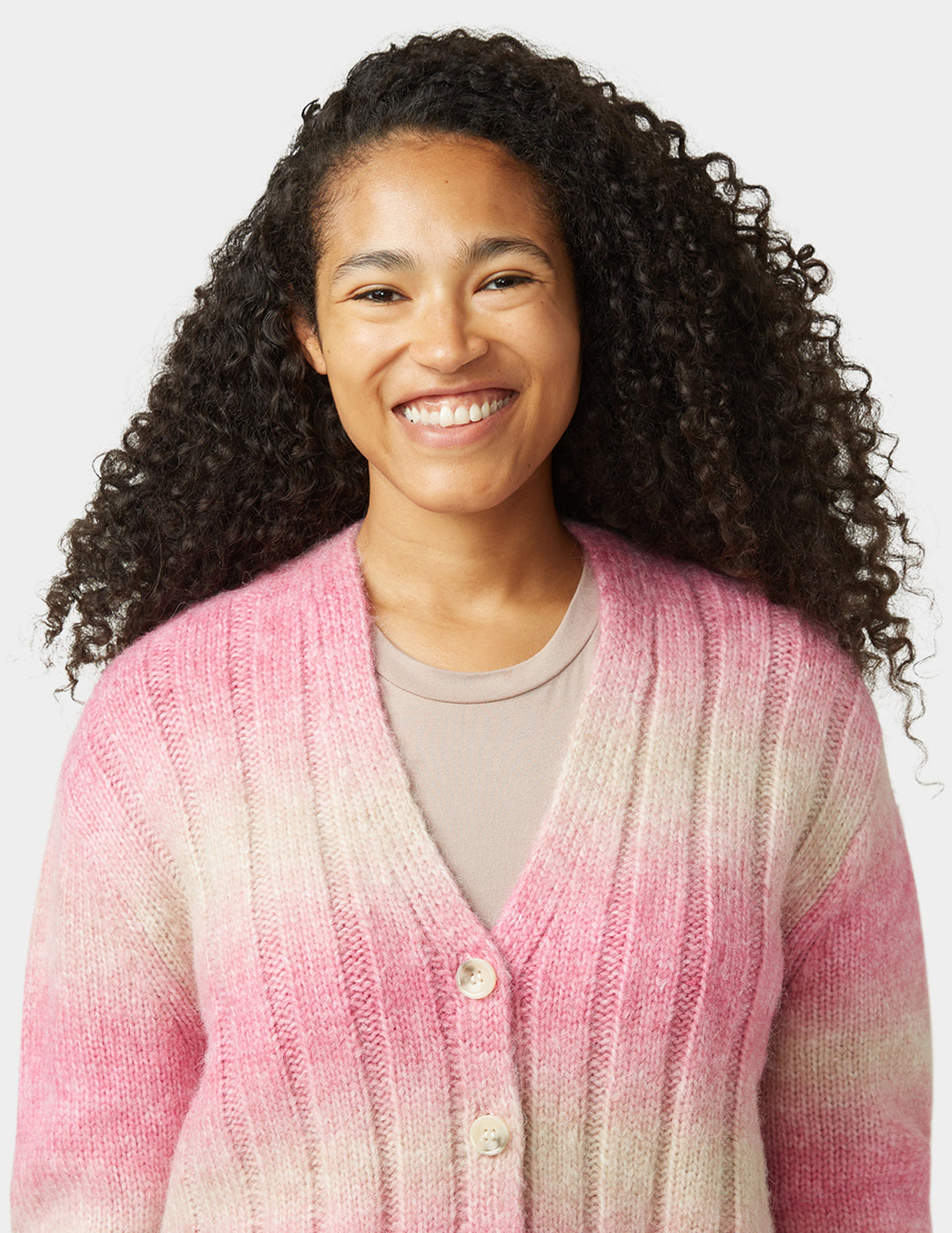 Woman wearing a pink and white gradient cardigan on a plain background