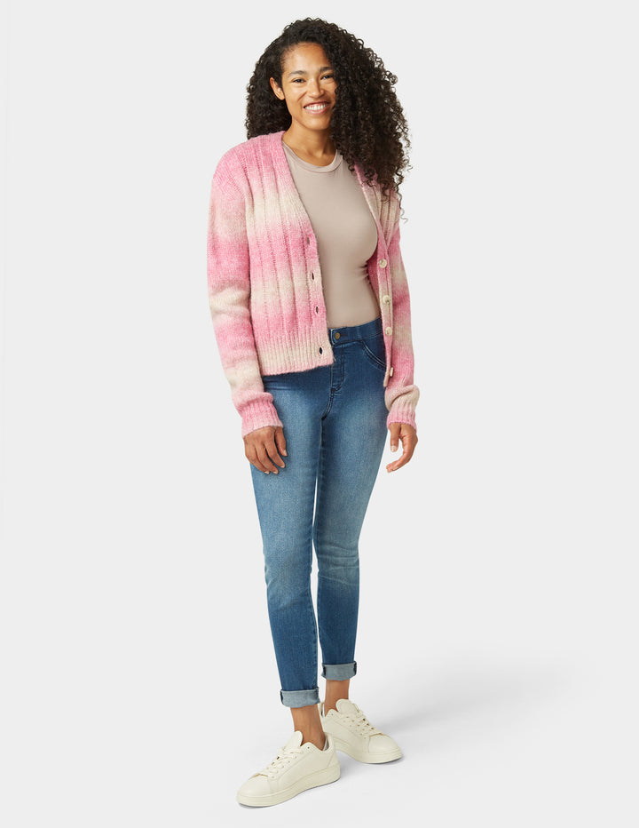 Woman wearing a pink and white striped cardigan, beige top, blue jeans, and white sneakers on a white background