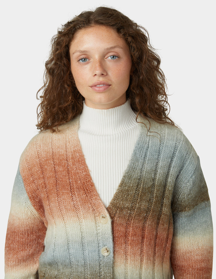 Woman wearing a colorful cardigan over a white turtleneck on a plain background