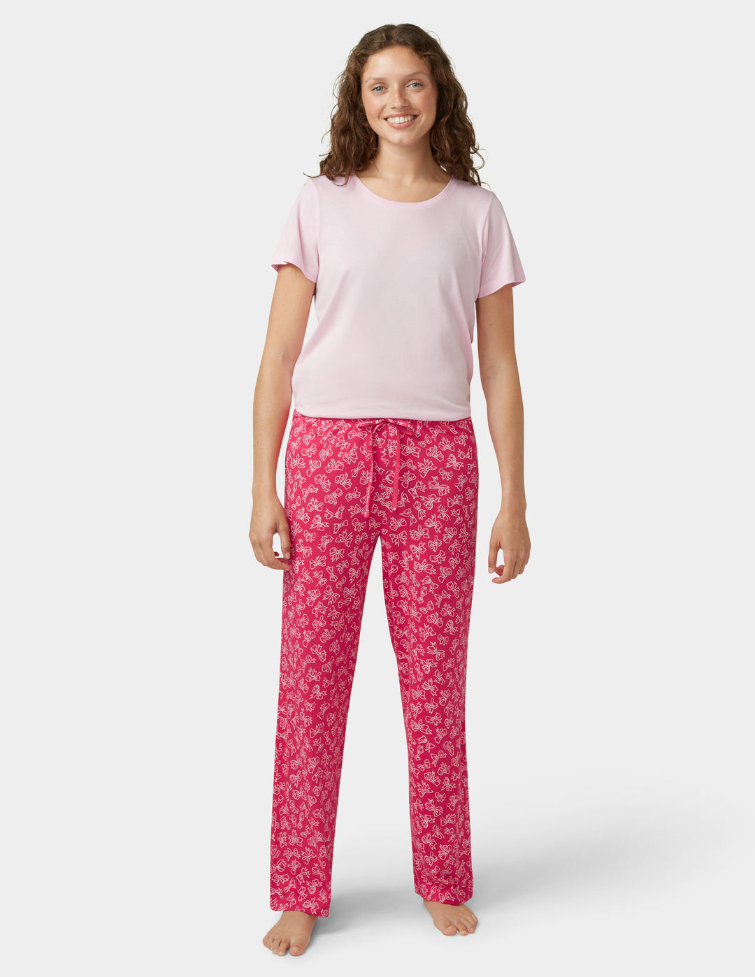 Woman wearing pink pajama top and red patterned pants on a white background