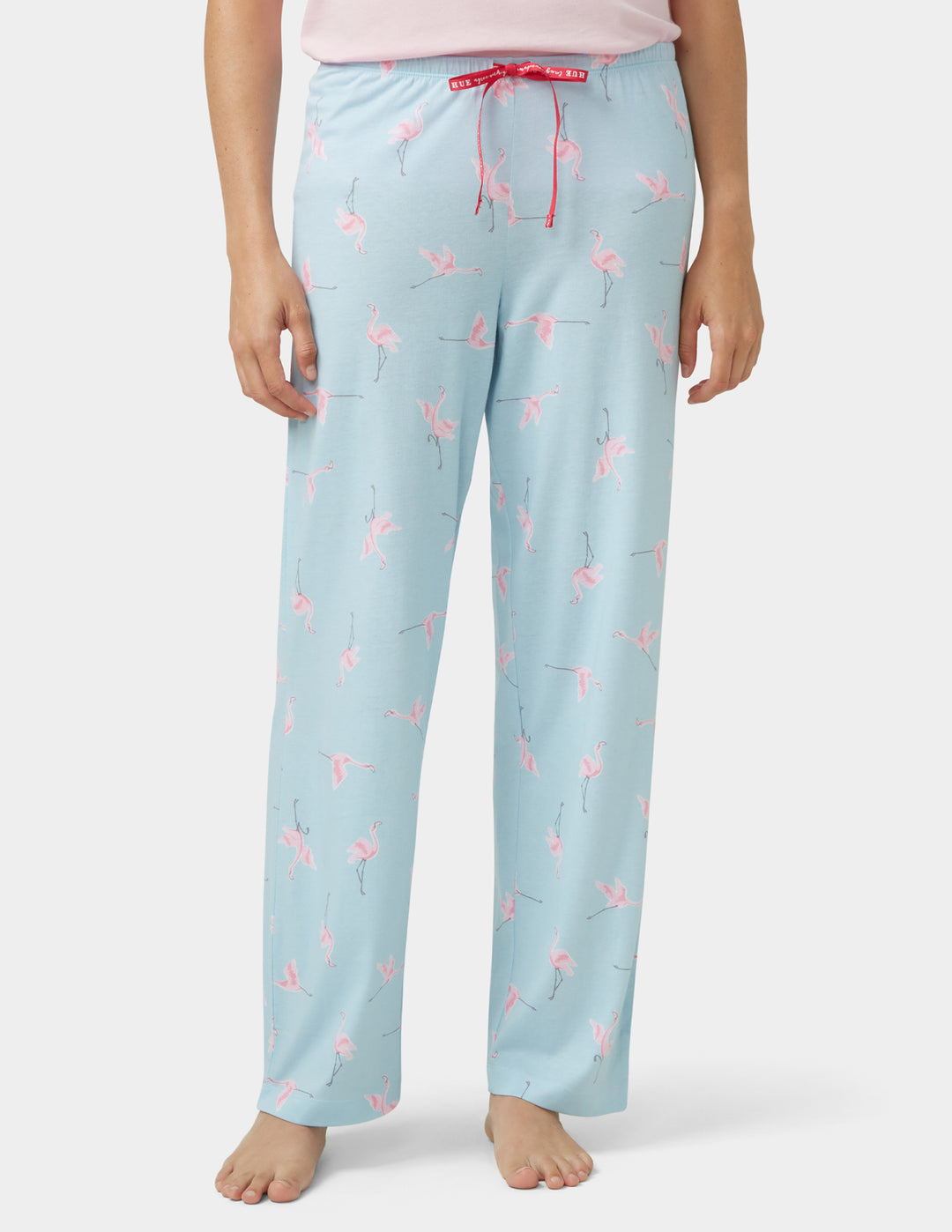 Light blue pajama pants with pink flamingo pattern worn by a person on a white background