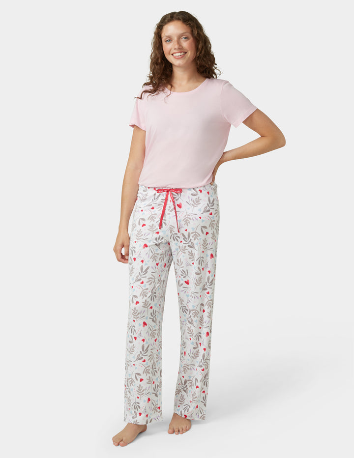 Woman wearing a pink top and patterned pajama pants on a white background
