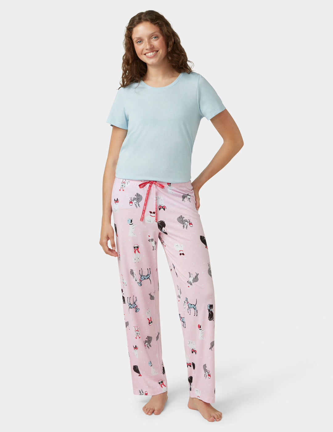Woman wearing a light blue t-shirt and pink pajama pants with animal print on a white background
