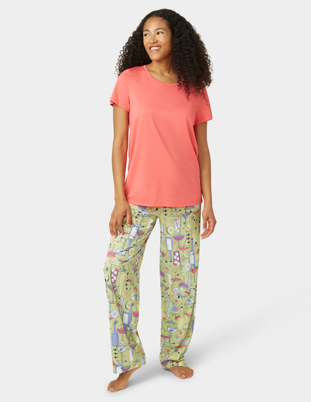 Woman wearing a coral top and patterned green pants on a white background