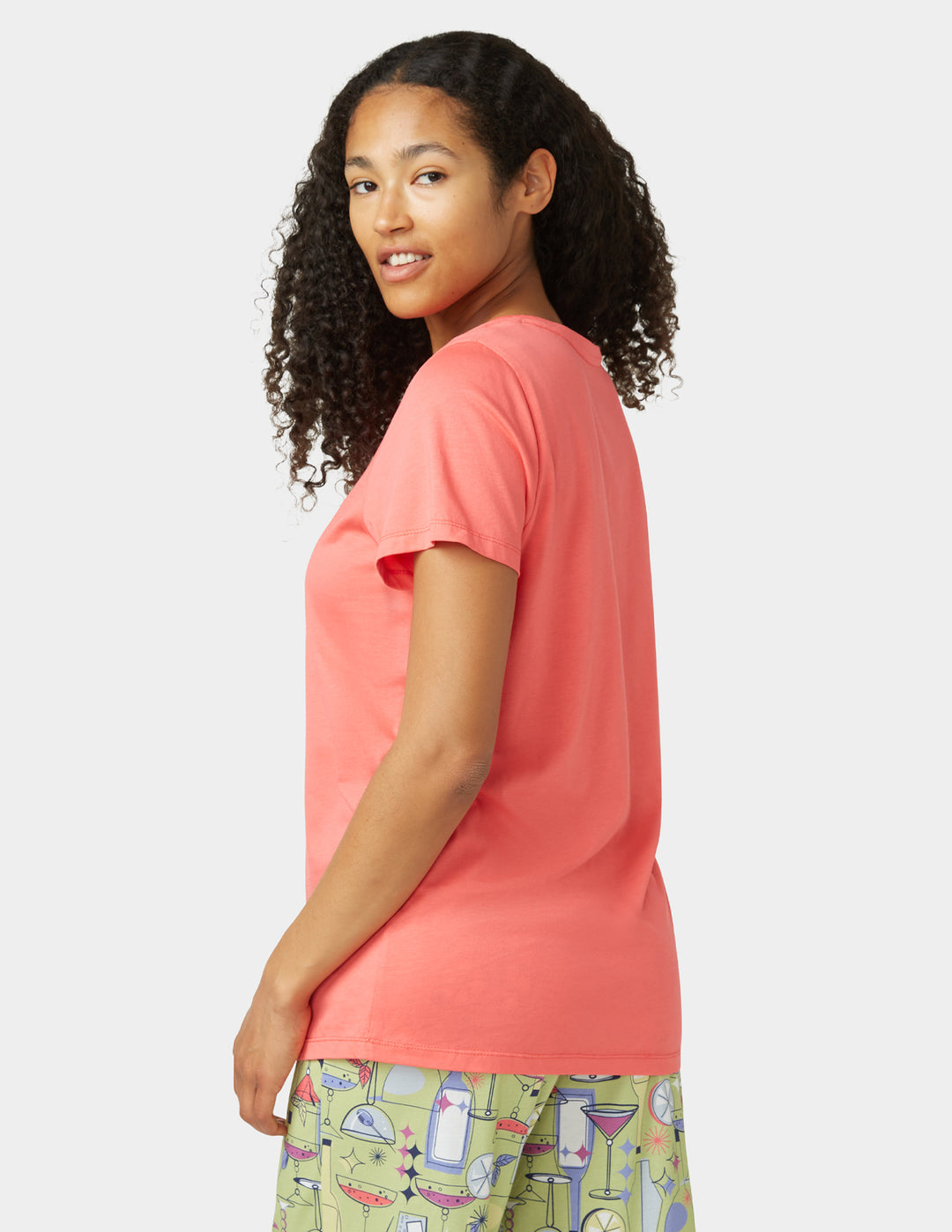 Woman wearing a coral t-shirt and patterned pants on a white background