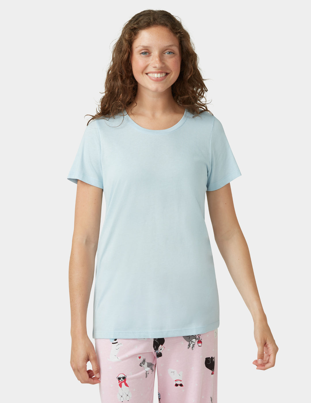 Woman wearing a light blue t-shirt and pink pajama pants with dog pattern on a white background