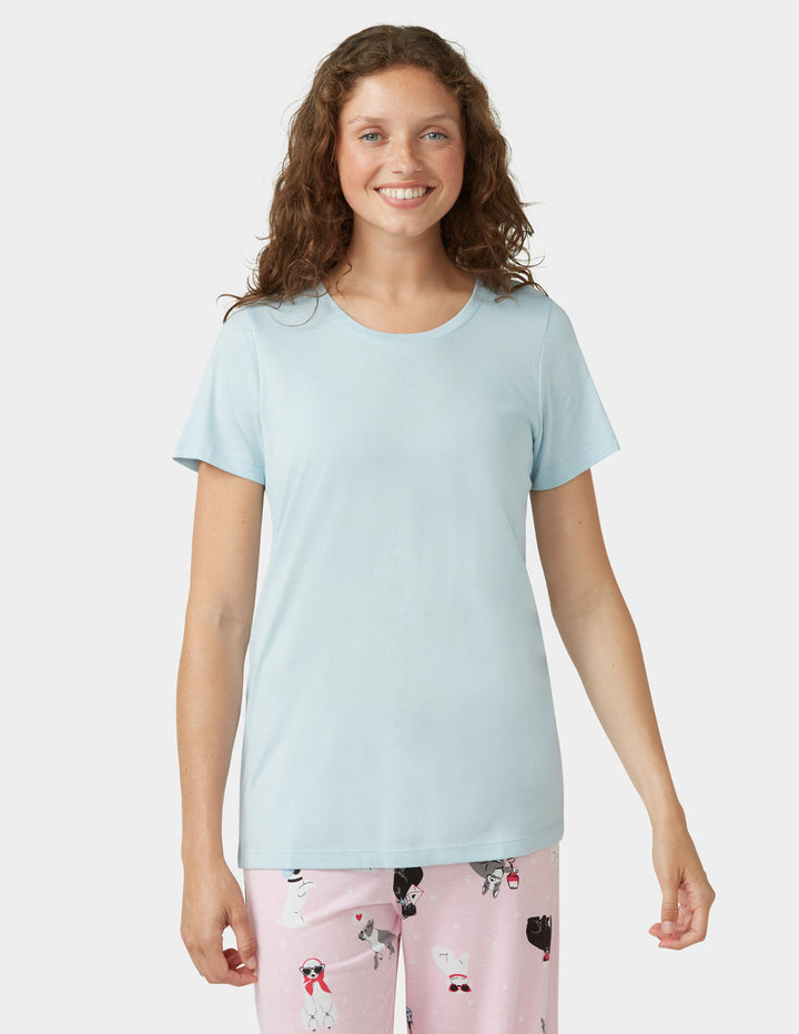 Woman wearing a light blue t-shirt and pink pajama pants with dog pattern on a white background