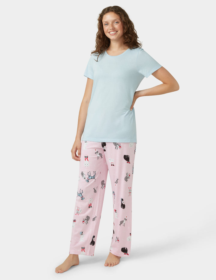Woman wearing a light blue t-shirt and pink pajama pants with cat print on a white background