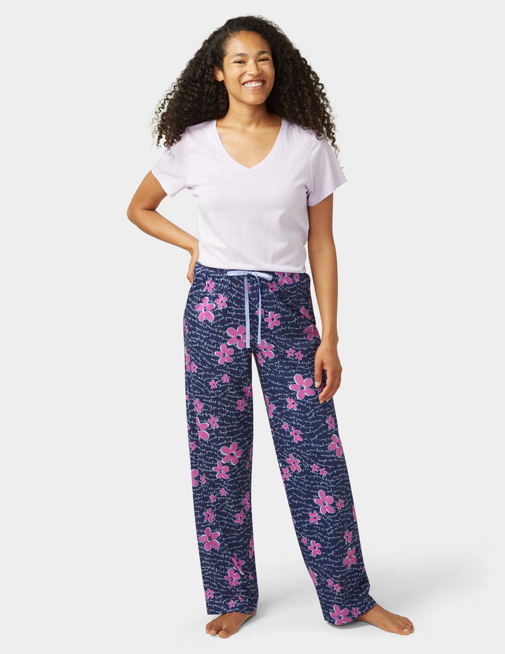 Woman wearing a white t-shirt and navy blue floral pajama pants on a white background