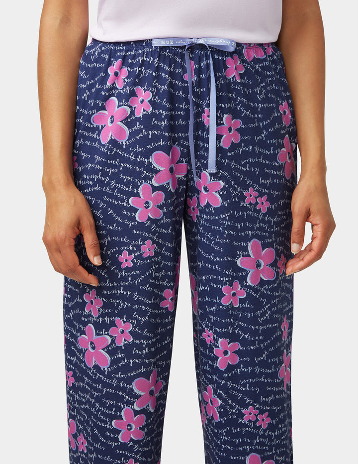 Navy blue pajama pants with pink floral patterns and white text worn by a person.