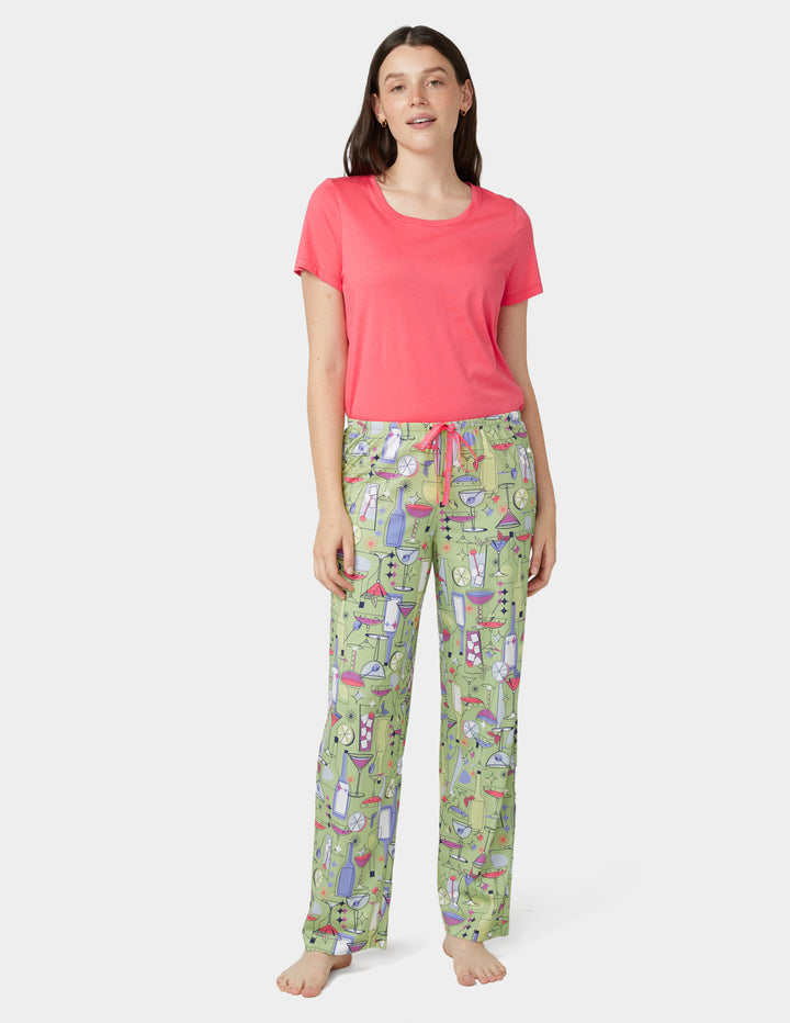 Woman wearing a pink top and green cocktail patterned pj pants on a white background