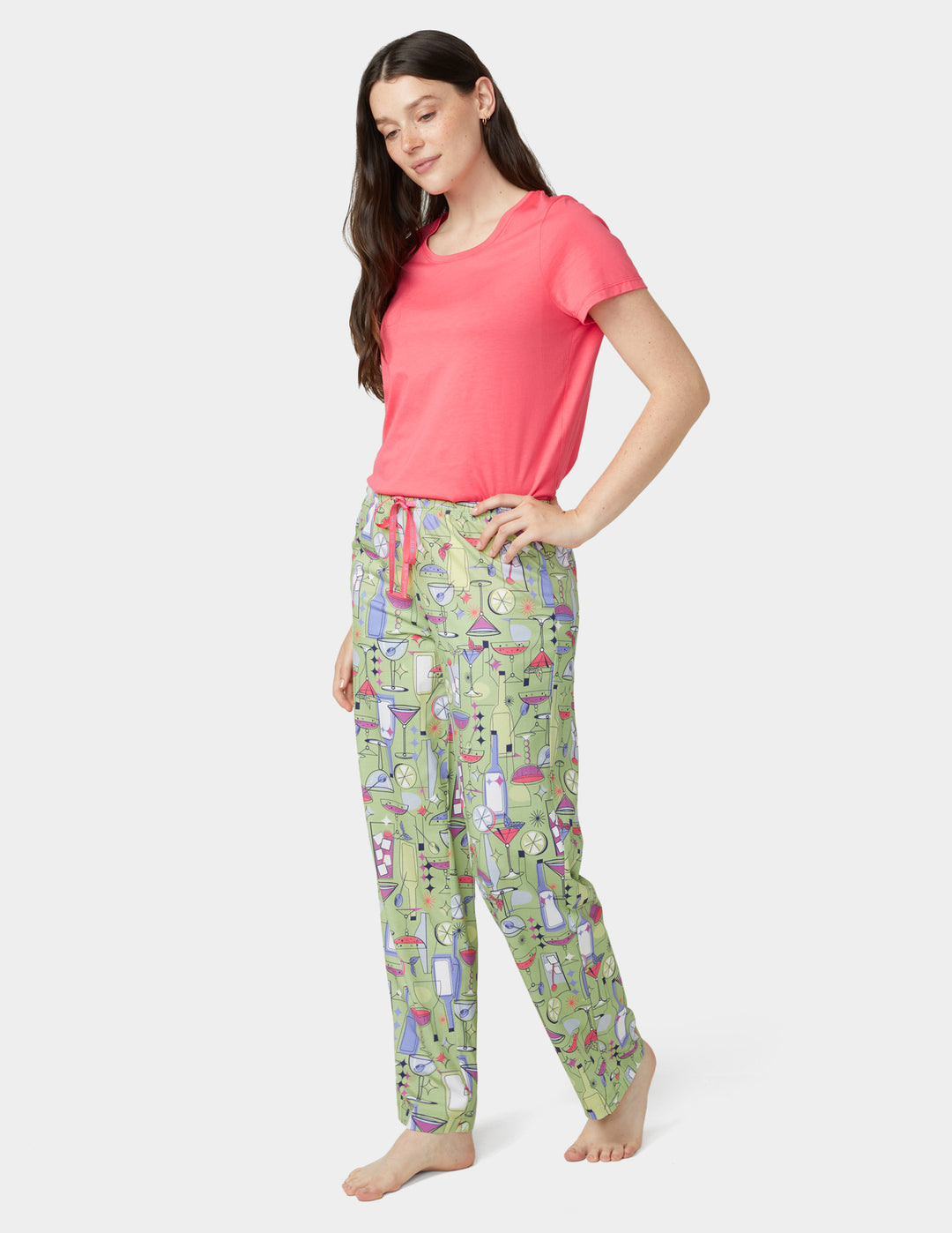 Woman wearing a pink top and patterned green pajama pants on a white background