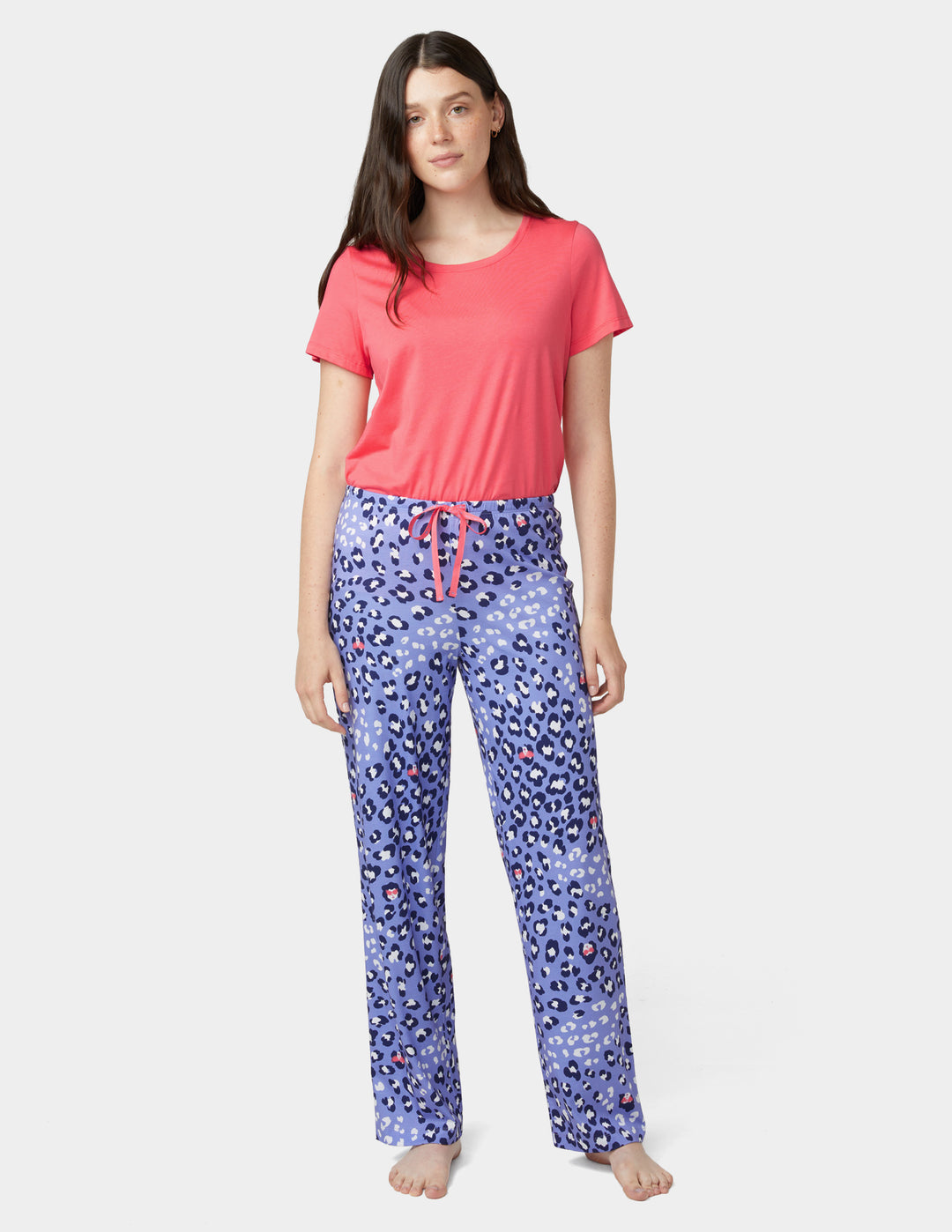Woman wearing a pink top and blue floral pajama pants on a white background