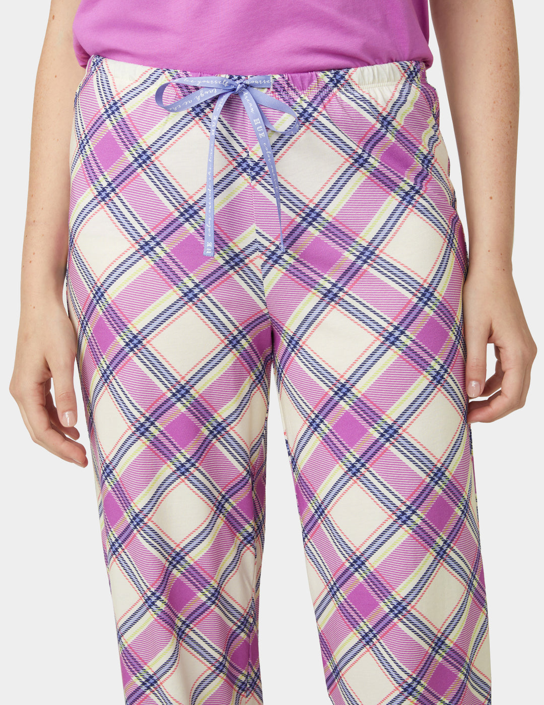 Person wearing pink and white plaid pants with a purple top on a white background