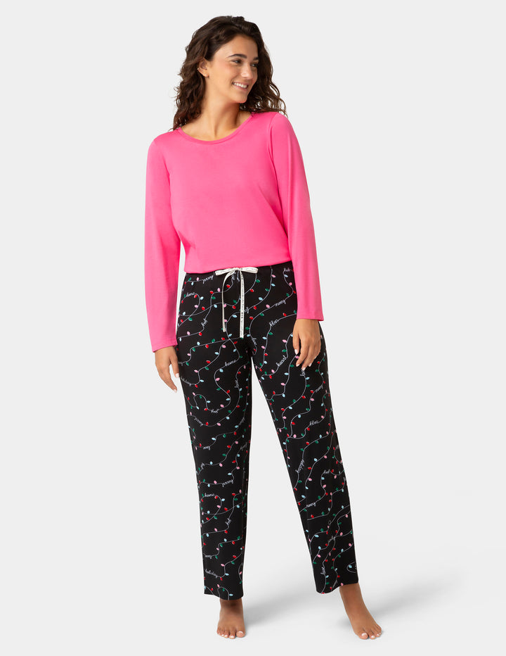 Woman wearing a pink long-sleeve top and black patterned pants on a white background
