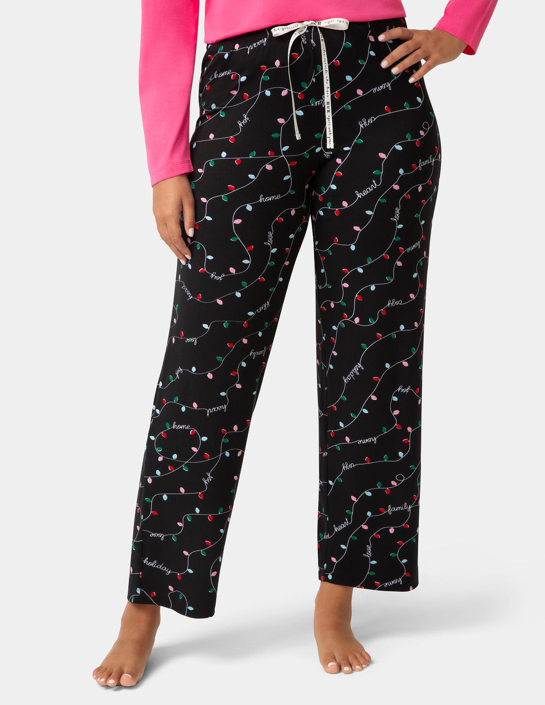 Black pajama pants with colorful Christmas light patterns worn by a person on a white background
