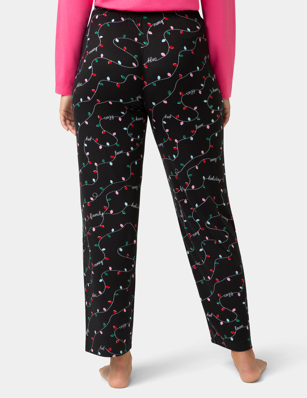 Black pajama pants with colorful Christmas light print worn by a person on a white background