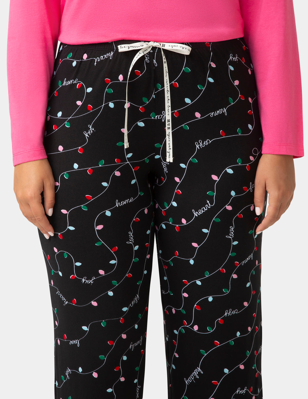 Black pajama pants with colorful light bulb pattern worn with a pink top on a white background