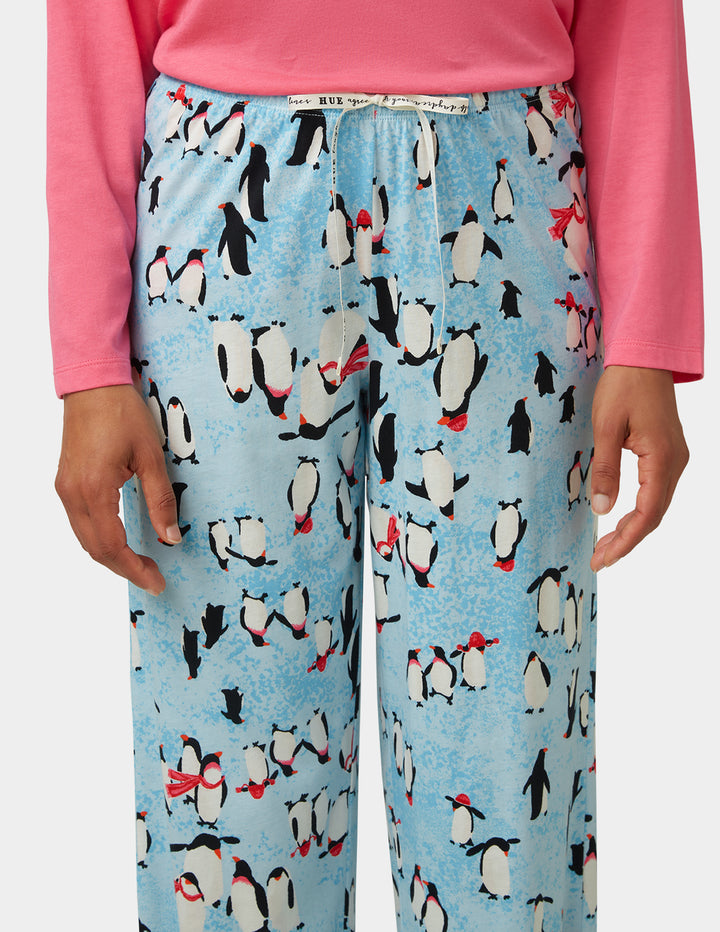 Pajama pants with penguin pattern worn by a person in a pink shirt.