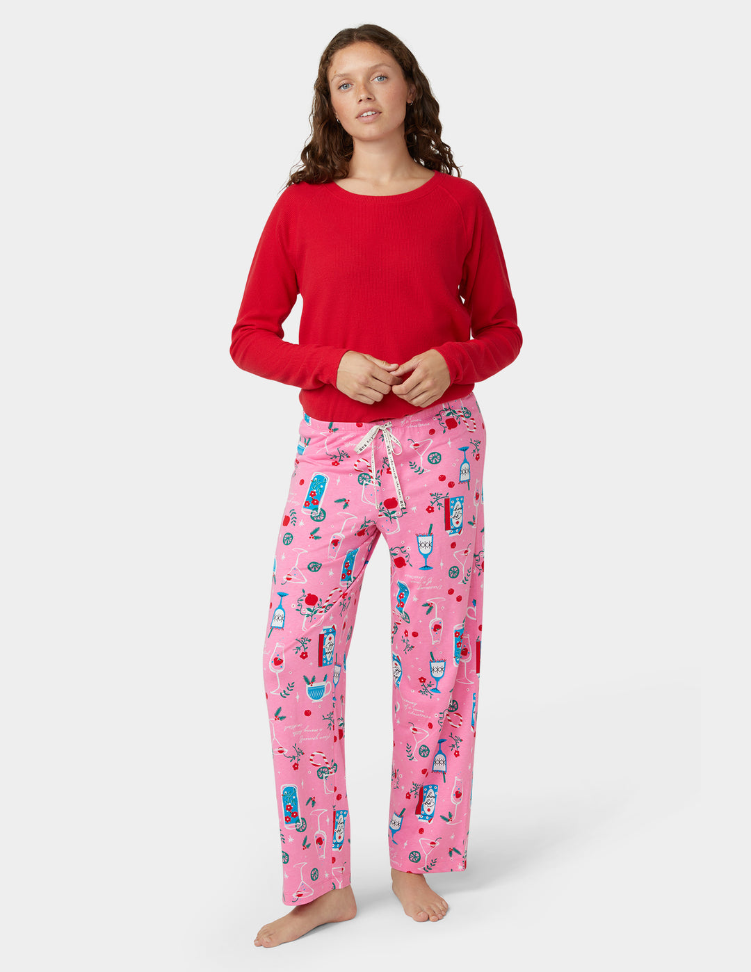 Woman wearing a red top and pink pajama set with holiday cocktail designs on a white background