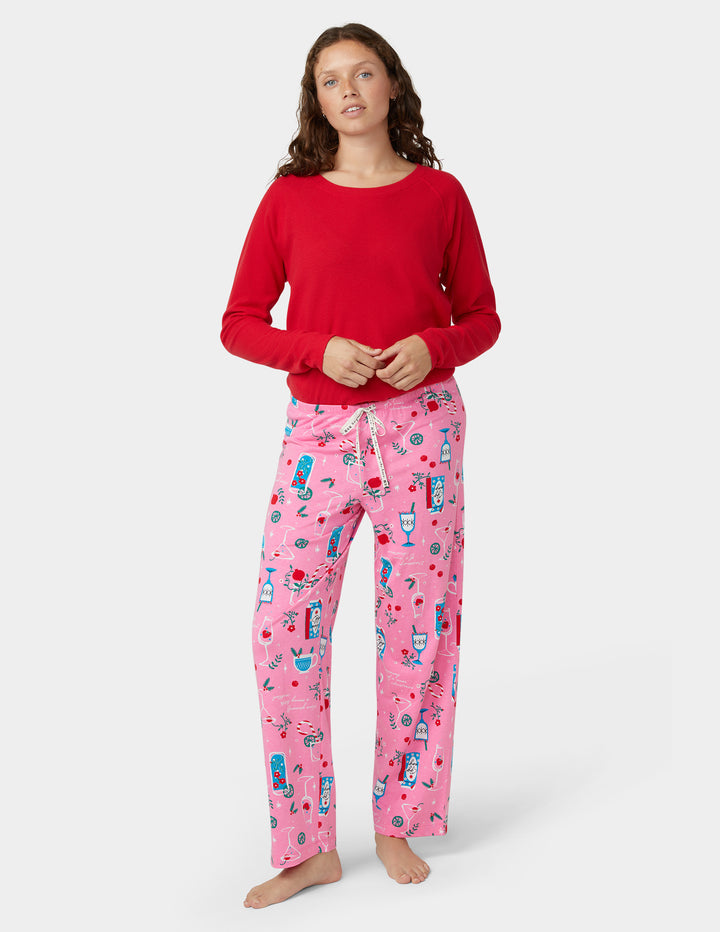 Woman wearing a red top and pink pajama set with holiday cocktail designs on a white background