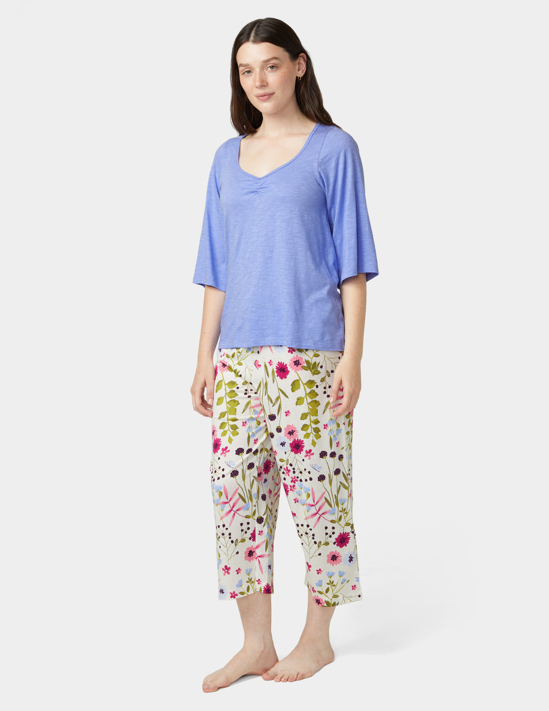 Woman wearing a blue top and floral capri pants on a white background
